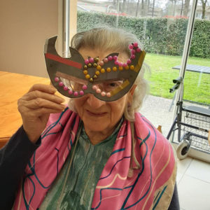 Une dame assise porte un masque de Carnaval sur le visage